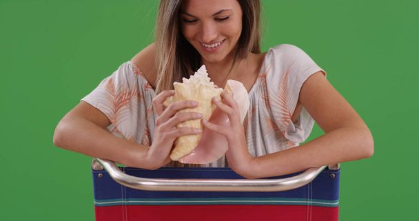 Millennial woman sitting in beach chair holding conch shell on green screen - Photo, image