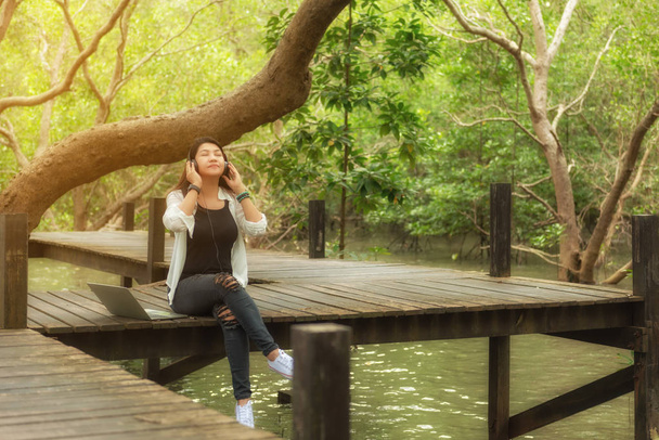Kadın dinlenmek ve kulaklık ve dizüstü doğa yeşil park, kız mutlu ile müzik dinleme sırasında bir kitap okuma. Yaşam tarzı ve tatil kavramı - Fotoğraf, Görsel