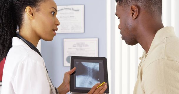 Potilas, jolla on niskakipua, keskustelee naislääkärin kanssa tabletin röntgenkuvasta
 - Valokuva, kuva