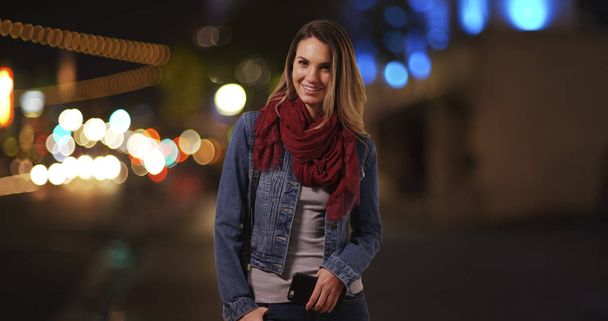 Millennial Girl steht abends mit Handy auf der Straße in der Innenstadt - Foto, Bild