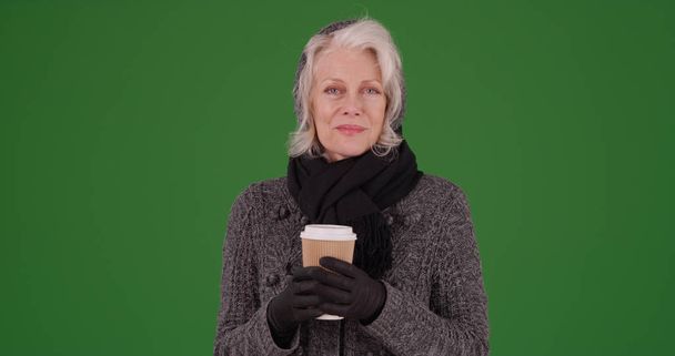 Szép magas rangú női téli ruhában, tartja a kávét a zöld képernyő - Fotó, kép