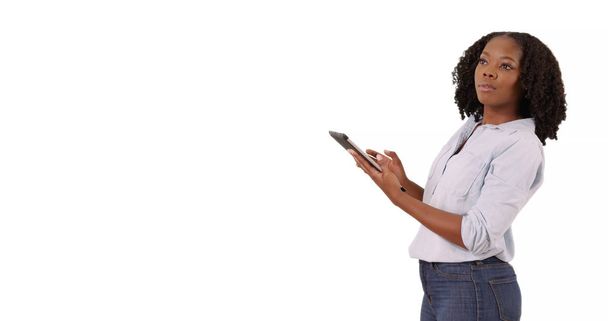 Attractive black woman in shirt and jeans using tablet in studio with copyspace - Фото, зображення