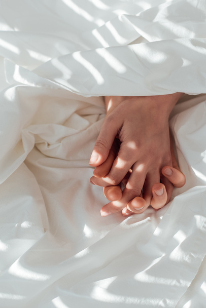 partial view of loving couple holding hands while lying under blanket together - Φωτογραφία, εικόνα