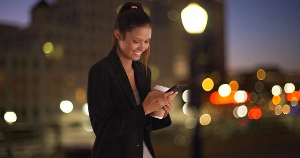 Biznes kobieta tekst wiadomości na telefon komórkowy, podczas gdy centrum w mieście w nocy - Zdjęcie, obraz