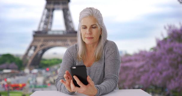 Eiffel Tower yakınındaki masada oturan smartphone büyük beyaz kadın denetler - Fotoğraf, Görsel