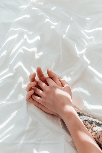 vista parziale di coppia amorevole che si tiene per mano mentre sdraiato su lenzuolo bianco
 - Foto, immagini