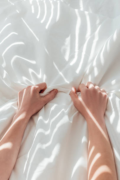 partial view of woman holding white bed sheet while lying in bed - Fotó, kép