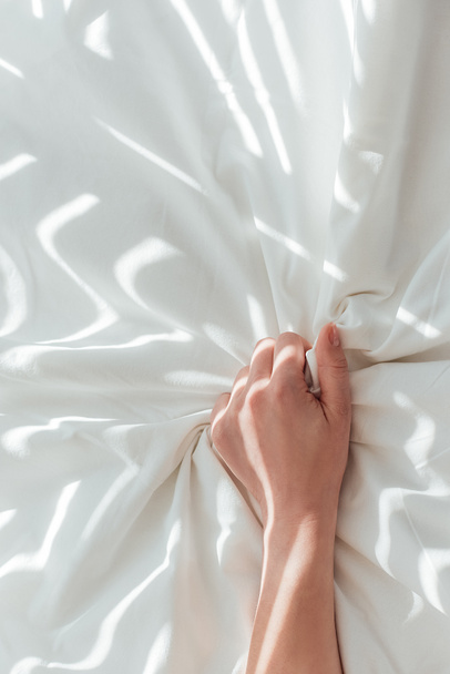 partial view of woman holding white bed sheet while lying in bed - Foto, Bild