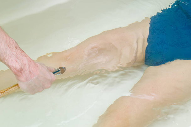 Woman in bath during hydromassage in beauty spa salon. Underwater hydrotherapy massage procedure - Foto, afbeelding