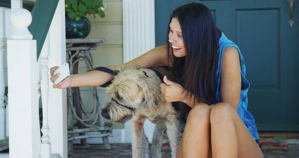Mujer de raza mixta sentada en el porche tomando fotos con el perro
 - Foto, imagen