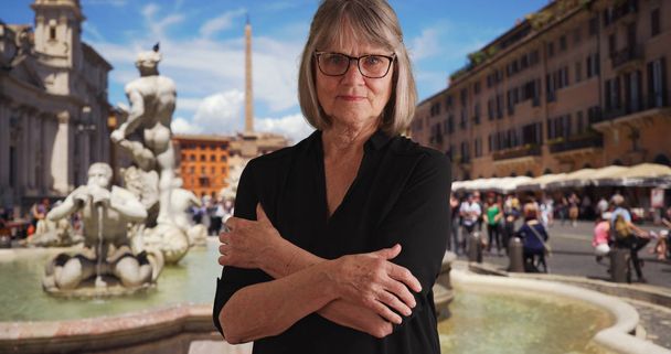 腕を組んで厳しくローマの噴水近く探している深刻なシニア女性 - 写真・画像