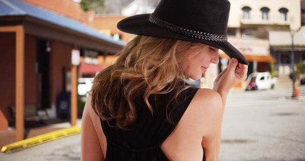 Sarışın beyaz bir kadın geri kamera için gün boyunca alışveriş bölgesi içinde siyah şapka modelleme - Fotoğraf, Görsel