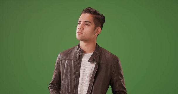 Hombre hispano guapo en chaqueta de cuero de pie mirando en serio en la pantalla verde
 - Foto, Imagen