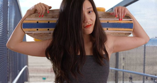 Hipster femme millénaire portant skateboard sur les épaules à la plage
 - Photo, image