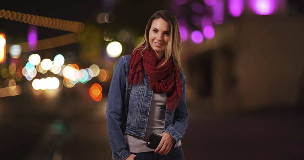 Millennial tyttö seisoo kadulla keskustassa pitäen matkapuhelin illalla
 - Valokuva, kuva