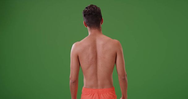 Vista posteriore dell'uomo latino in costume da bagno guardando in lontananza sullo schermo verde
 - Foto, immagini