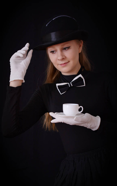 Actress in black hat and black suit holding a tea pair - Фото, изображение