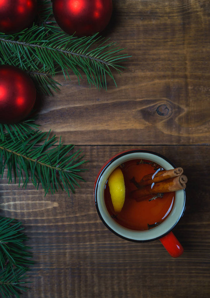 Cup of hot aromatic tea with cinnamon sticks and lemon with Christmas tree branches and red balls on wooden table background. Christmas New Year winter holiday concept. Flat lay, top view - Foto, afbeelding