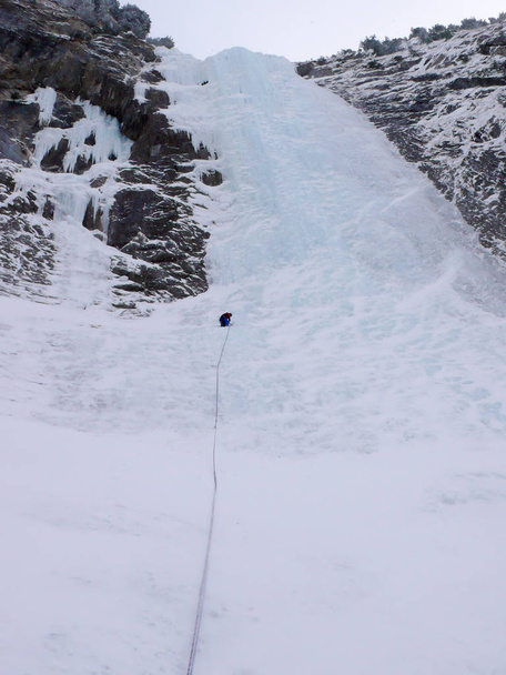 mannelijke bergbeklimmer ijs het beklimmen van een steile en lange bevroren waterval in de Zwitserse Alpen in de diepe winter - Foto, afbeelding