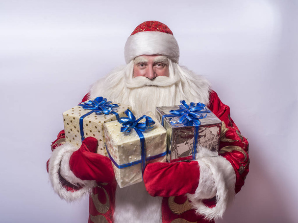 Funny and funny Santa Claus on a gray background congratulates and gives a lot of gifts - Photo, Image
