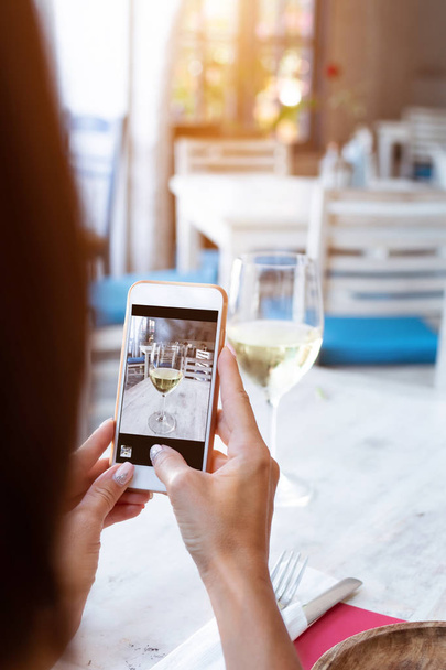 Vrouw nemen foto van witte wijn op haar smartphone in restaurant. - Foto, afbeelding