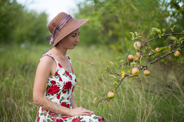 kaunis tyttö seisoo omena puutarha tausta. Tyttö on pukeutunut kesämekkoon
. - Valokuva, kuva