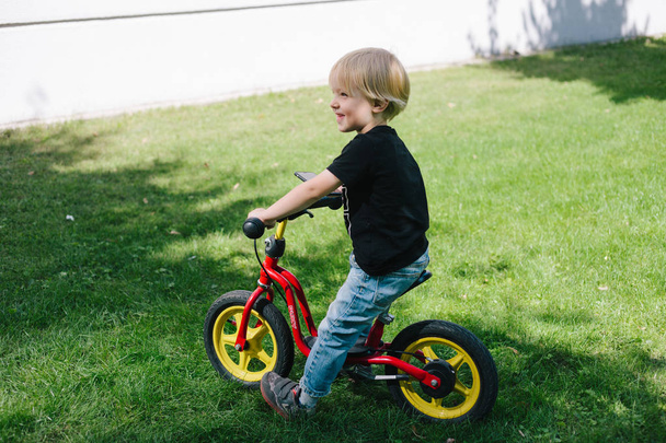 3 years old happy toddler boy riding red bike. Little kid learns to ride a bicycle. Sport, cycling, active playing, and childhood concept - 写真・画像