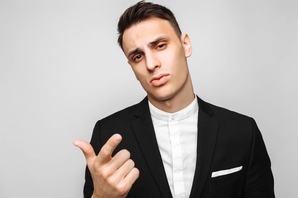 Handsome young business man, male, in a classic black suit, points the finger at the camera, against a gray background. Business concept, career. - Foto, Bild