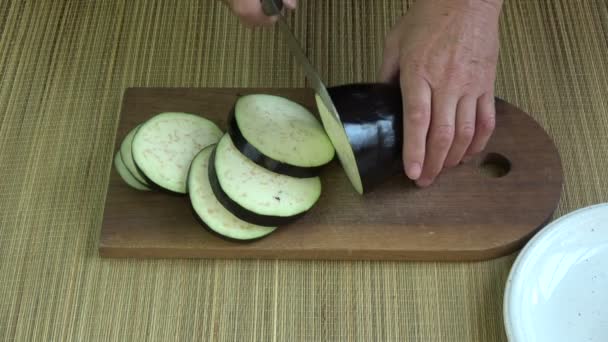 Tagliare melanzane fresche su tavola di legno in cucina - Filmati, video
