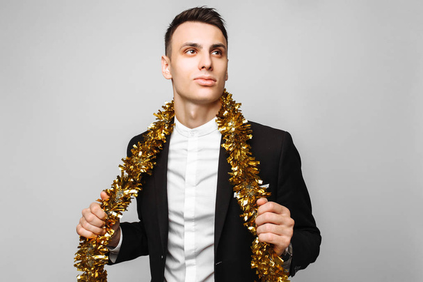 attractive man in a business suit and with a tinsel around his neck, on a gray background. The concept of the new year. - Фото, изображение