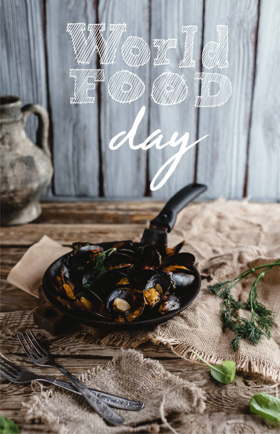 gourmet fried mussels with shells on frying pan and forks on table, world food day lettering - Photo, Image