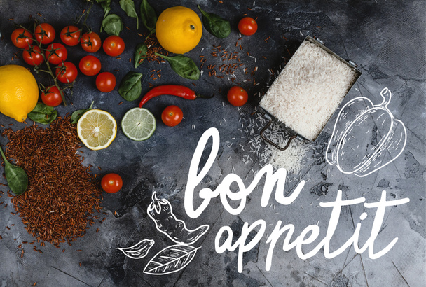 top view of raw rice in container, spices and vegetables on scratched grey surface, bon appetit lettering - Photo, Image
