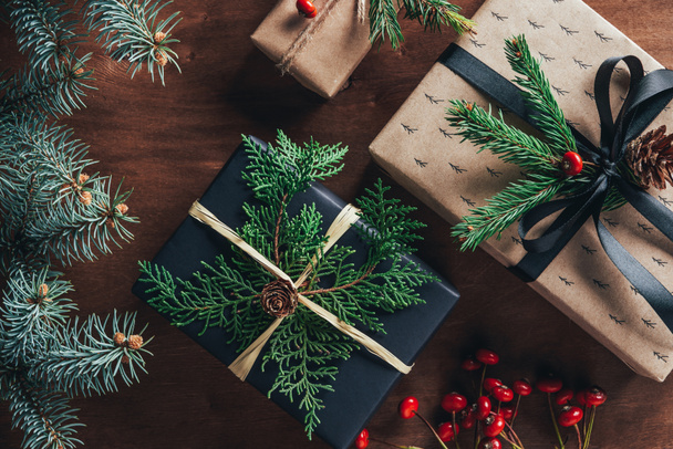 верхний вид рождественских подарочных коробок с еловыми ветвями и декоративными ягодами на деревянном фоне
   - Фото, изображение
