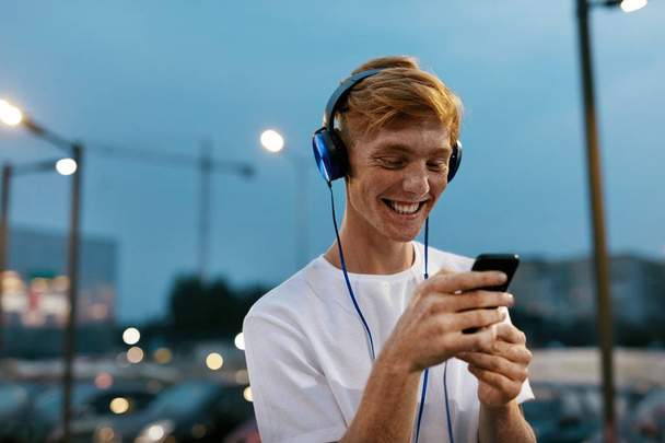 Man In Headphones Using Mobile Phone At City Street - 写真・画像