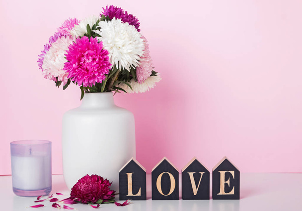 Flowers in a vase and word Love arranged from wooden letters near the pink wall - Foto, Imagem