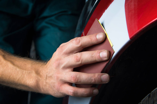 Grinder papier in handen van een man die een lak van de auto in de auto-winkel verscherpen. - Foto, afbeelding