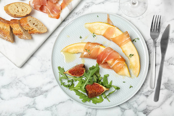 Flat lay composition with plate of melon slices and prosciutto on marble table - Fotoğraf, Görsel