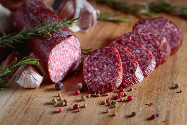 Gerookte salami op een oude houten tafel. Worst met rozemarijn, knoflook en peper. - Foto, afbeelding