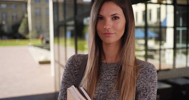 Portrait of smart young Caucasian female with books outside on university campus - Photo, Image