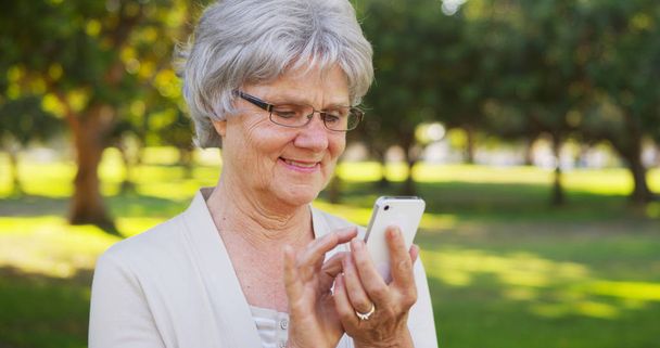 Mujer mayor mensajes de texto en el teléfono inteligente en el parque
 - Foto, Imagen
