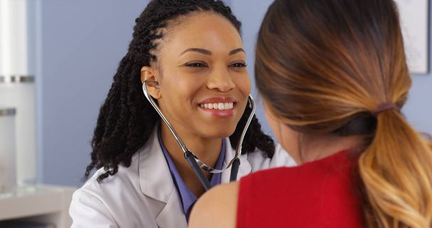 Close up of African American physician listening to heart and lungs of patient - Foto, afbeelding