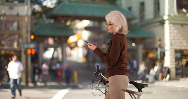 Mature Caucasian woman with bicycle using phone in Chinatown San Francisco - Photo, Image