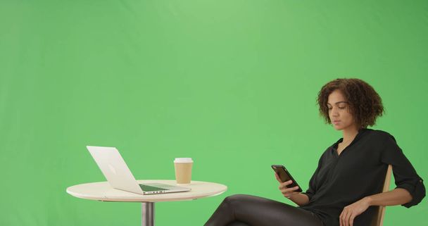 Egy fiatal fekete nő ül a kávézó asztal, ő a zöld képernyő telefon - Fotó, kép