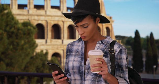 Afro-Amerikaanse vrouw in Rome maakt gebruik van telefoon terwijl het drinken van koffie in de buurt van Colosseum - Foto, afbeelding