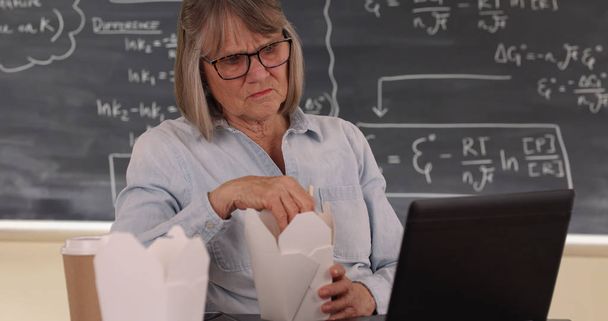 Öğle yemeği ve sınıfta dizüstü bilgisayar kullanan olgun beyaz kadın öğretmen - Fotoğraf, Görsel