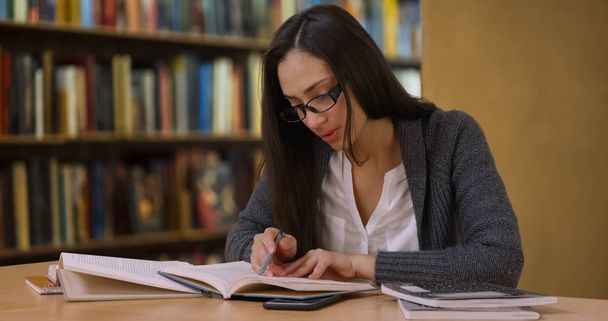 Atrakcyjna kobieta Hiszpanie w okularach czyta książkę w bibliotece - Zdjęcie, obraz