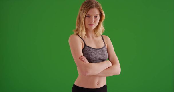 selbstbewusstes blondes Mädchen in Sportbekleidung posiert mit gefalteten Armen auf grünem Bildschirm - Foto, Bild