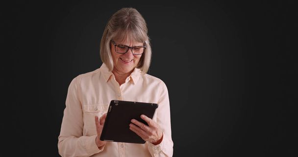 Gioioso ridere anziana donna godendo utilizzando pad dispositivo su sfondo grigio
 - Foto, immagini