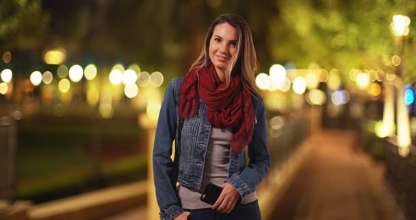 Trendy millennial girl standing with cellphone at park in the evening - Photo, Image