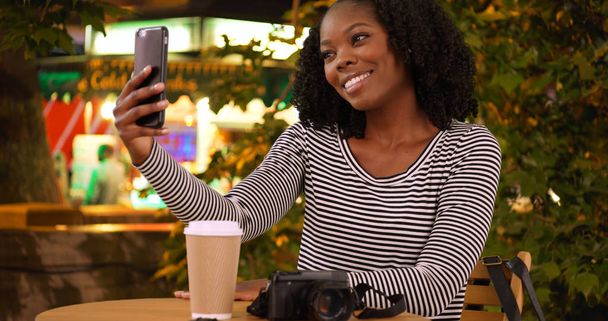 Χαριτωμένο μαύρη γυναίκα παίρνει μια selfie με έξυπνο τηλέφωνο κοντά σε περίπτερο τροφίμων τη νύχτα - Φωτογραφία, εικόνα